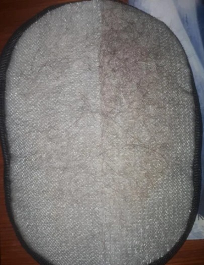 The underside of a hairpiece, showing dark hairs attached to a light gray mesh base.