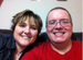 A smiling woman with short brown hair and a smiling man with glasses and a red shirt.