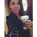 A woman with dark hair, wearing a patterned shirt, holds up a drink in a disposable cup.