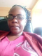 A slightly blurry close-up of a woman with glasses, wearing a pink shirt and a red jacket.