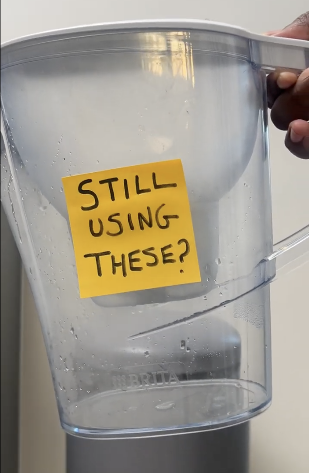 Clear water pitcher with a yellow note saying 'Still using these?'