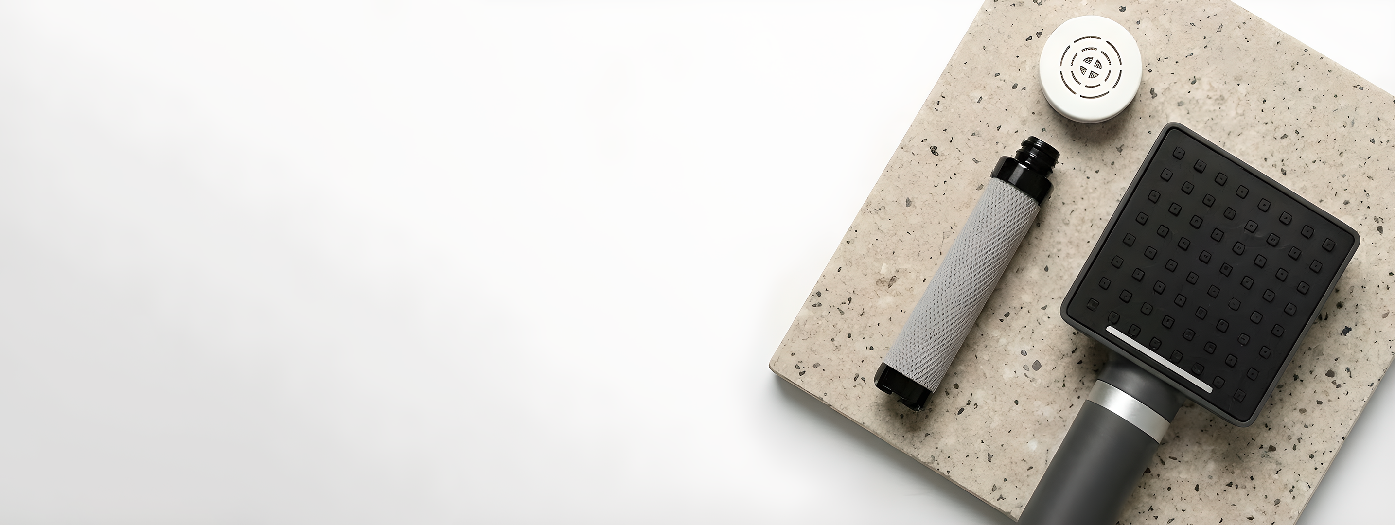 Square black showerhead on speckled stone surface with cylindrical object.