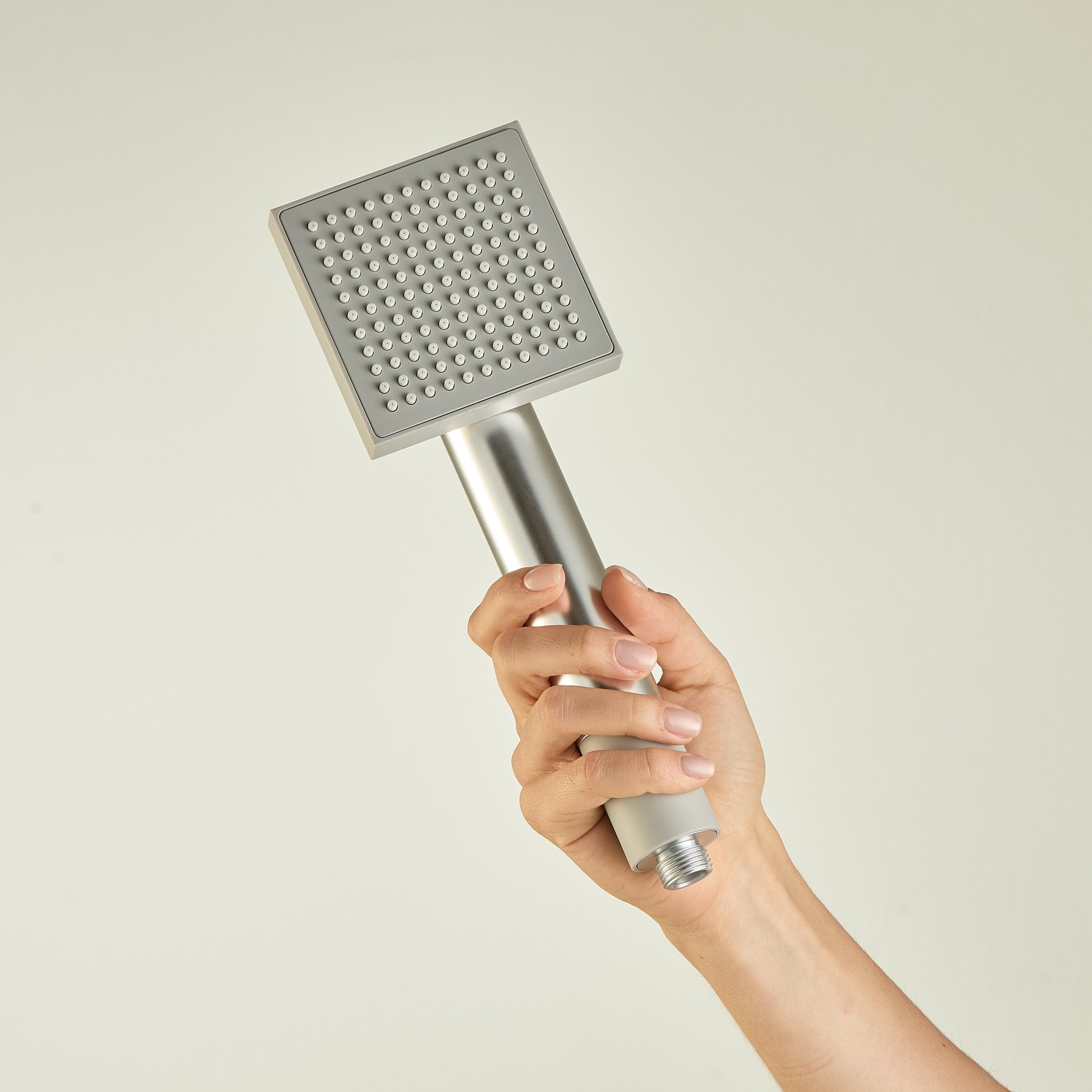 A hand holding the liquid chrome Water2skin handheld shower filter.