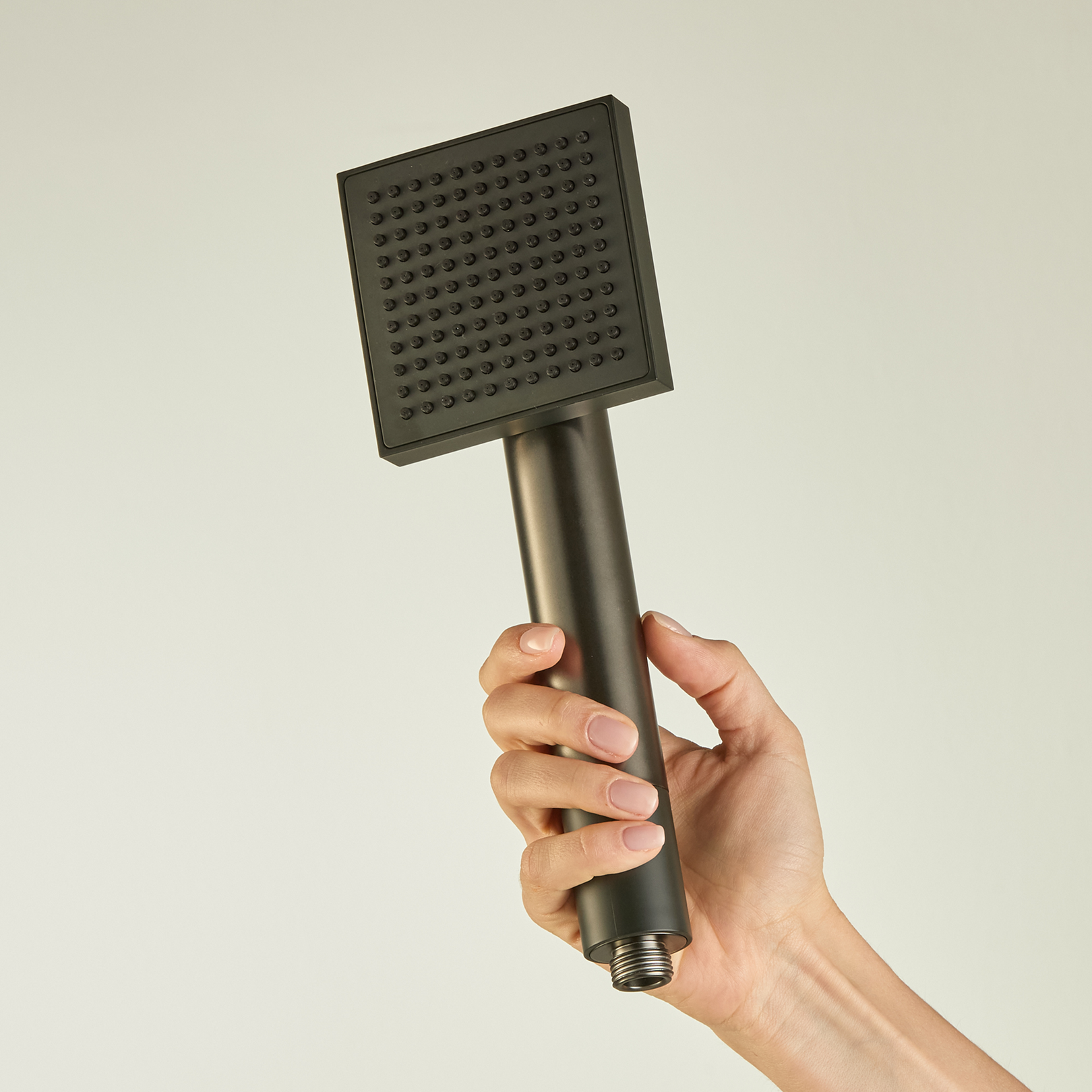 A hand holding a square, silver-colored handheld shower head against a plain background.