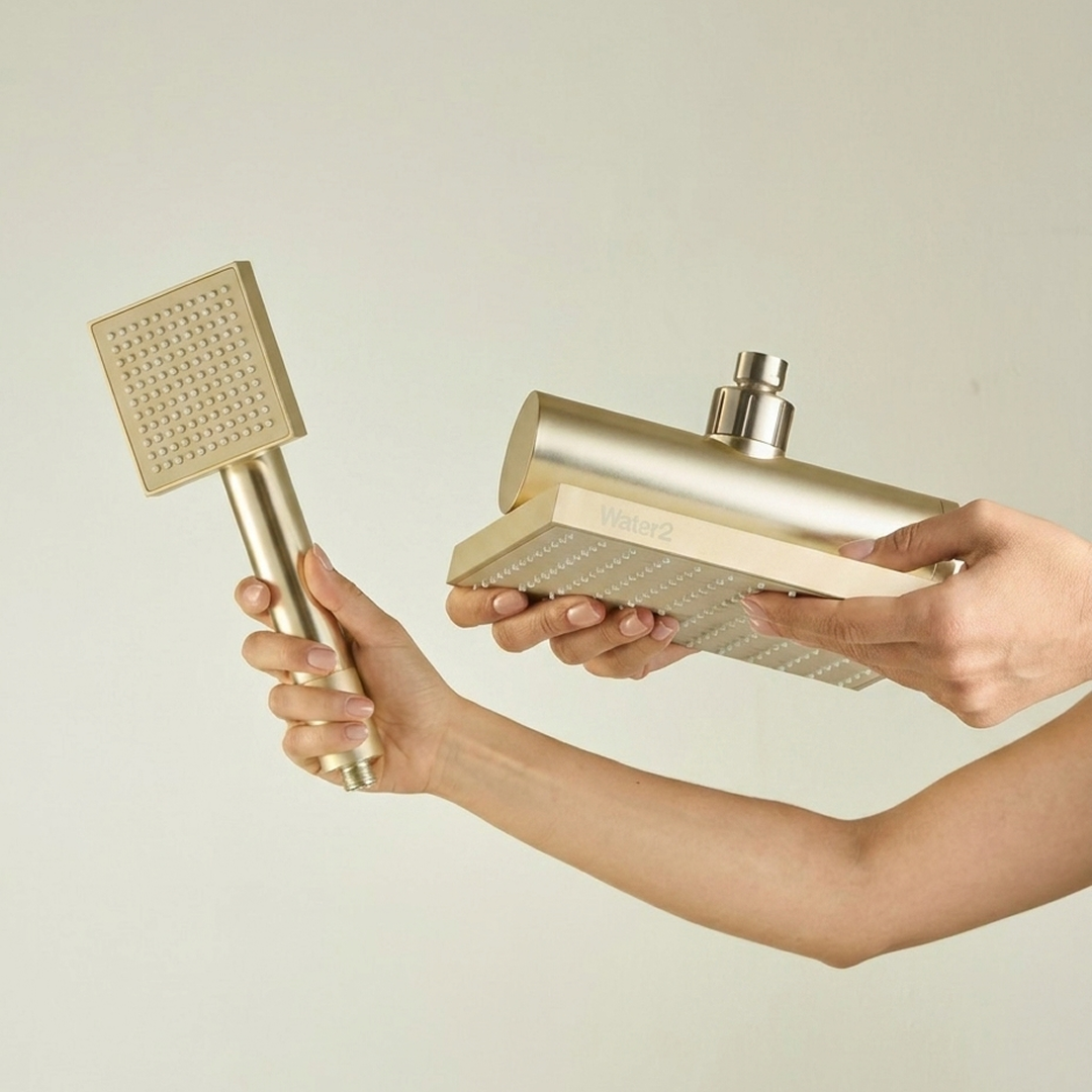 A pair of hands holding a matching gold-colored handheld shower wand and a rain shower head.