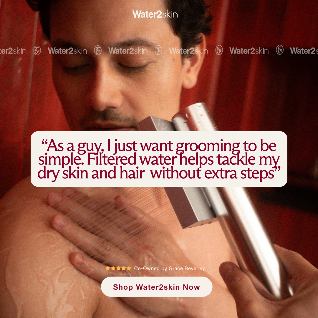 A man in a shower washes his shoulder with one hand while holding the shower head.
