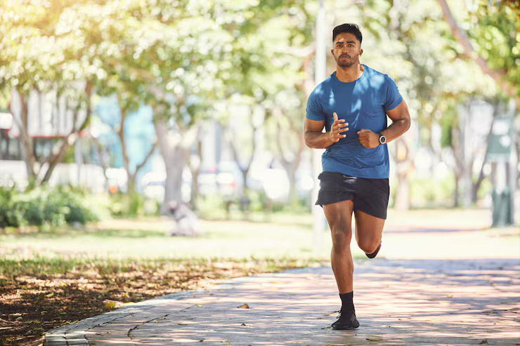A man in a blue t-shirt and black shorts runs on a paved path in a park.