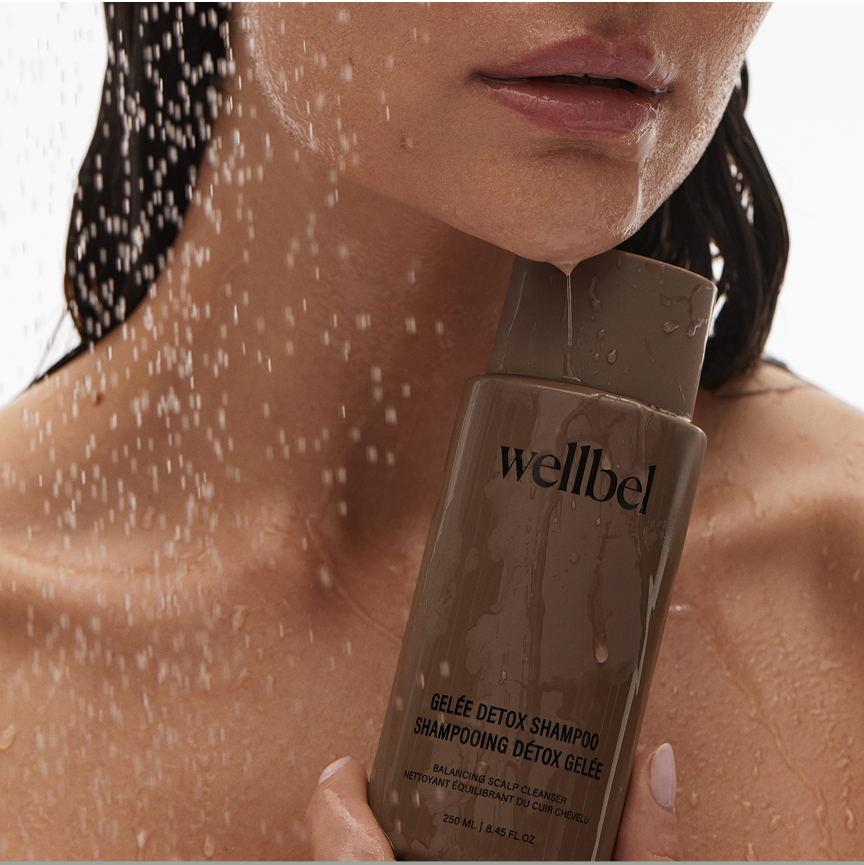 Person holding a bottle of Wellbel shampoo under running water.