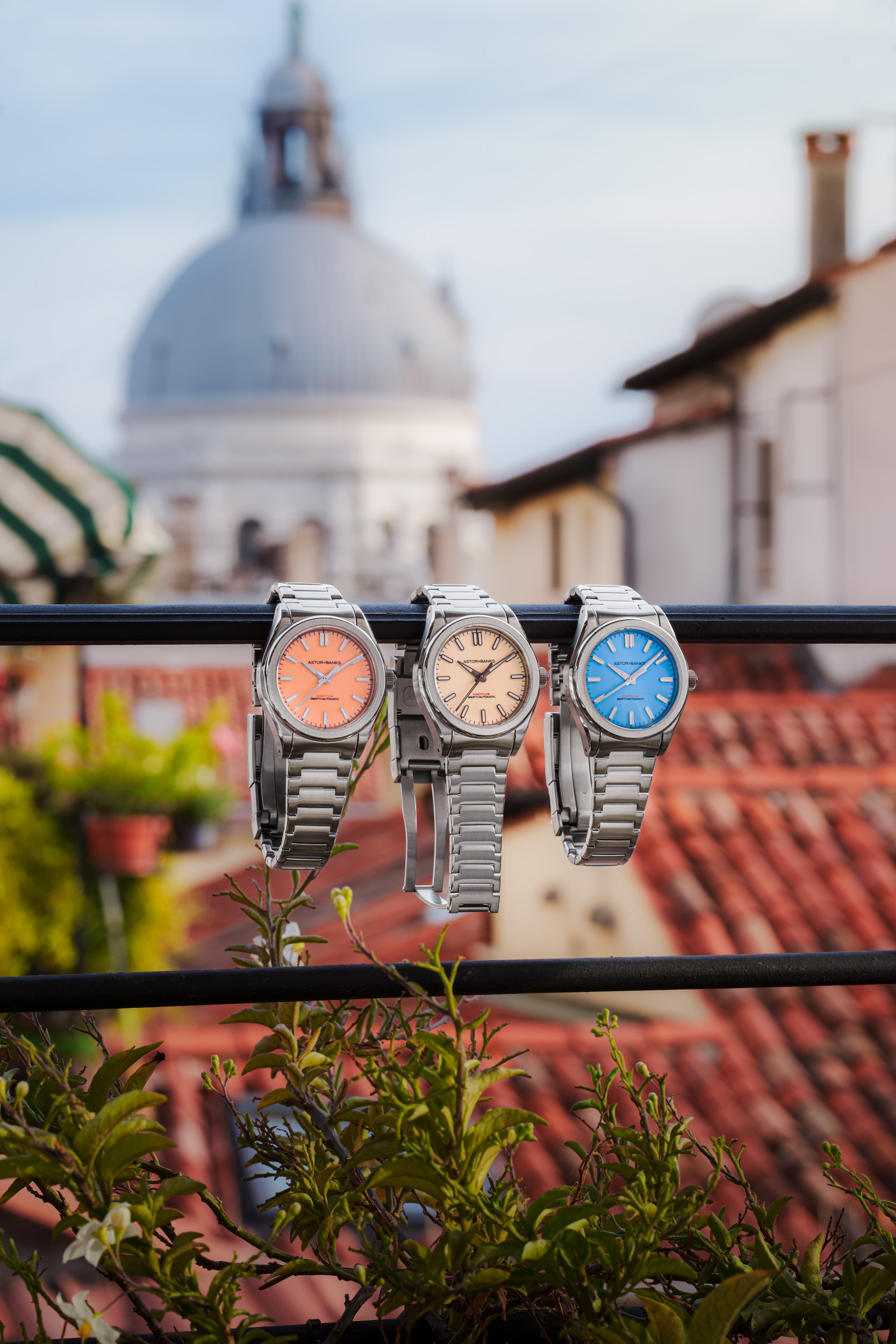 Three wristwatches with colorful faces rest on a railing overlooking red-tiled rooftops and a large dome.