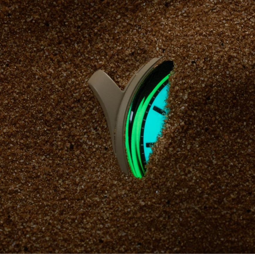 A glowing watch partially buried in sand.