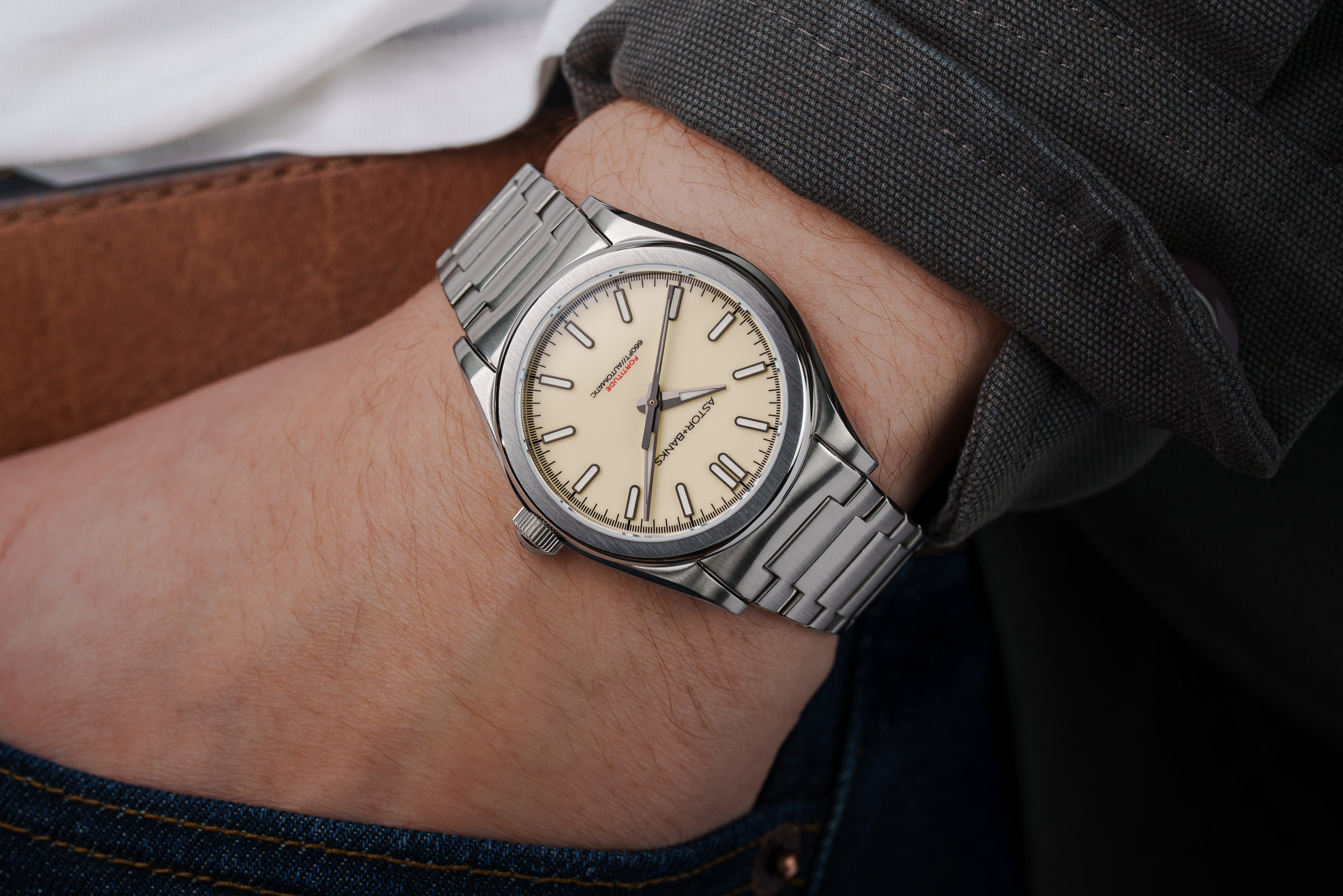 A close-up of a person's wrist wearing a stainless steel watch with a cream-colored dial.
