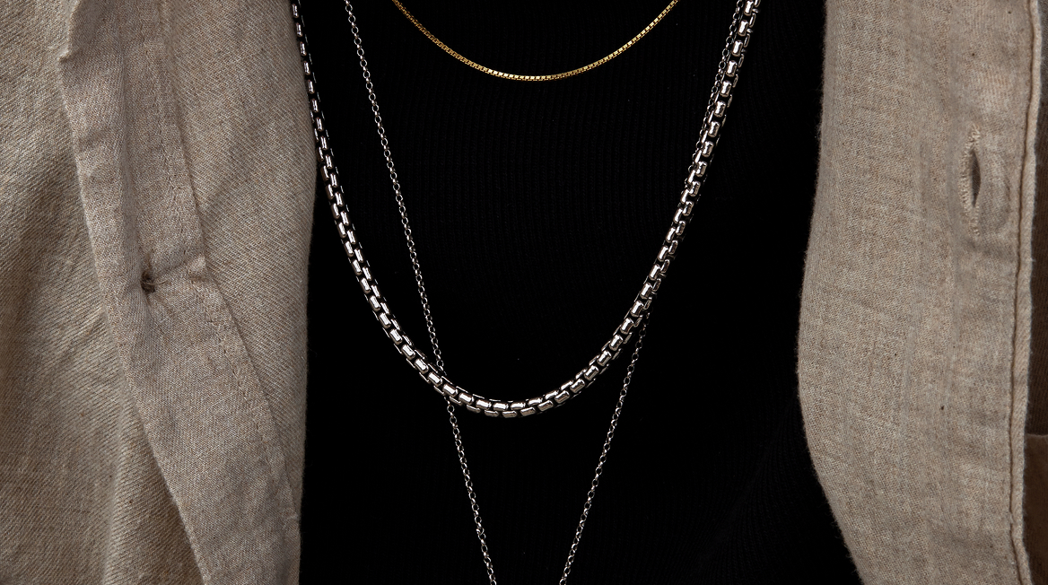 Close-up of layered necklaces on a black shirt with a beige jacket.