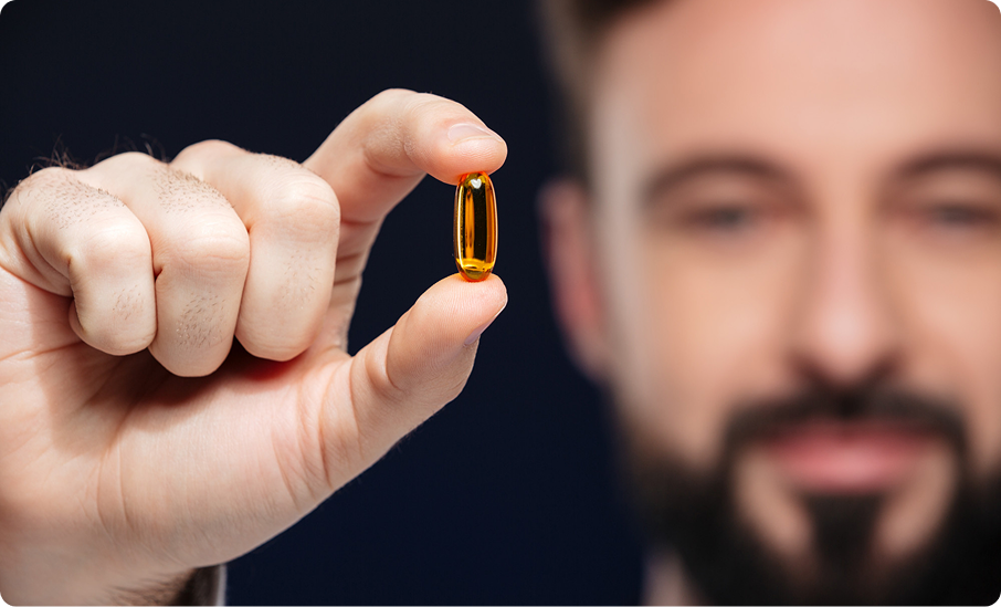 Person holding a yellow capsule between fingers, face blurred in background.