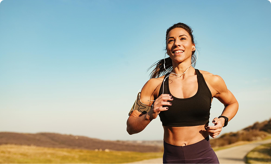 Woman jogging outdoors with earphones, wearing a black sports bra.