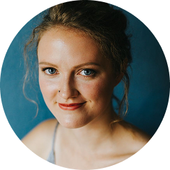 Young woman with curly hair smiling against a blue background.