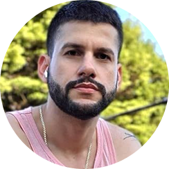 A person wearing a pink tank top and earbuds, outdoors with greenery in the background.