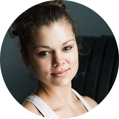 Person with curly hair wearing a white tank top, in front of gym equipment.