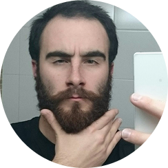 Man with a beard taking a selfie in a bathroom mirror.