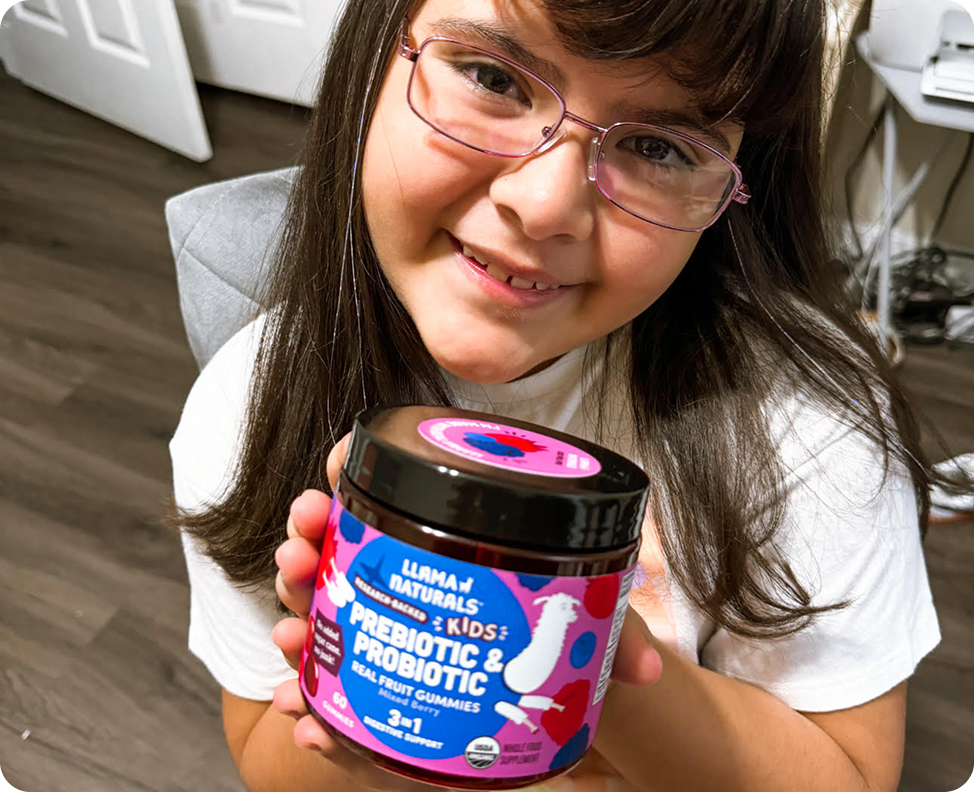 A smiling young girl with glasses holds up a jar of Llama Naturals Kids Prebiotic & Probiotic gummies.