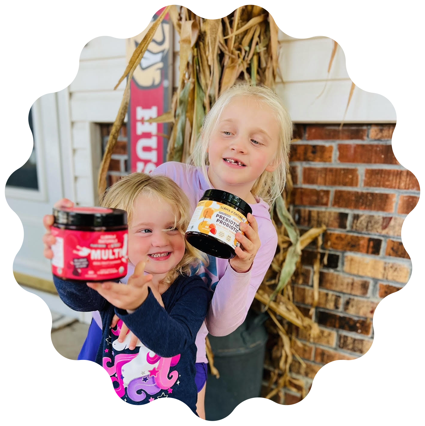 Two smiling young girls hold up jars of Llama Naturals supplements on a front porch.