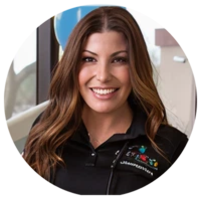 A headshot of a smiling woman with long brown wavy hair, wearing a black polo shirt.