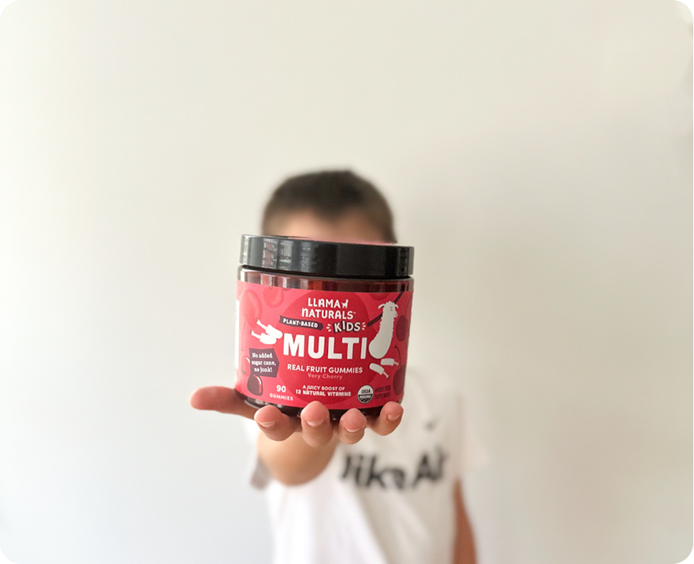 A child holds a jar of Llama Naturals Kids Multi gummies out toward the camera.