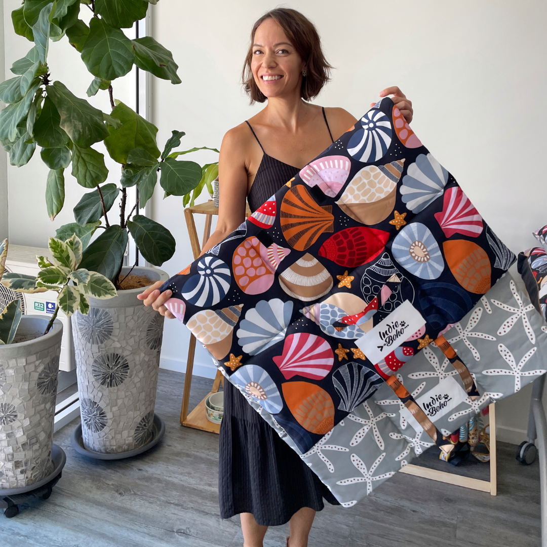 Person holding a colorful, patterned fabric with shell designs, standing next to potted plants.