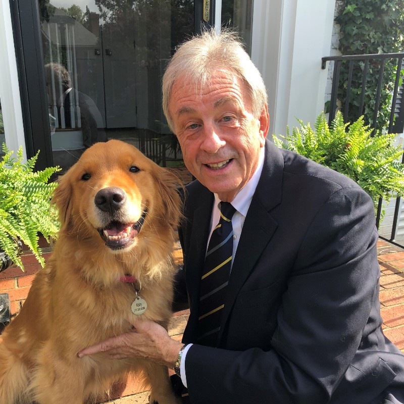 A man in a suit and tie smiles while kneeling next to a golden retriever.