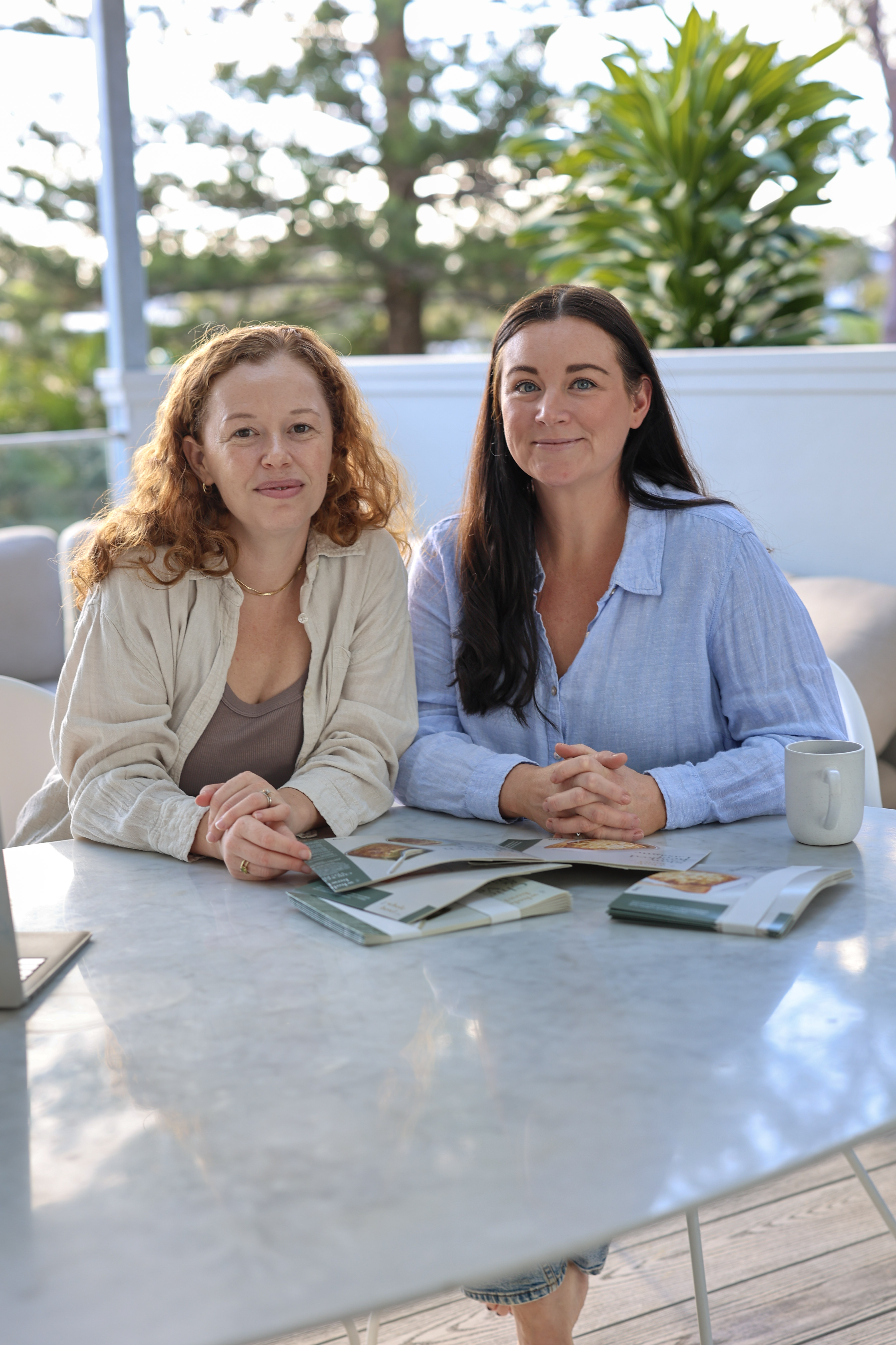 Two women sit at a marble table outdoors, looking toward the camera.