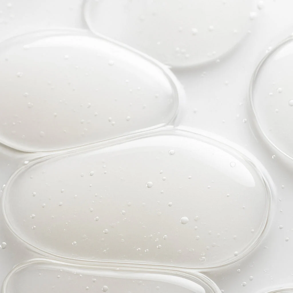 A close-up, macro shot of clear, gel-like blobs with bubbles on a white surface.