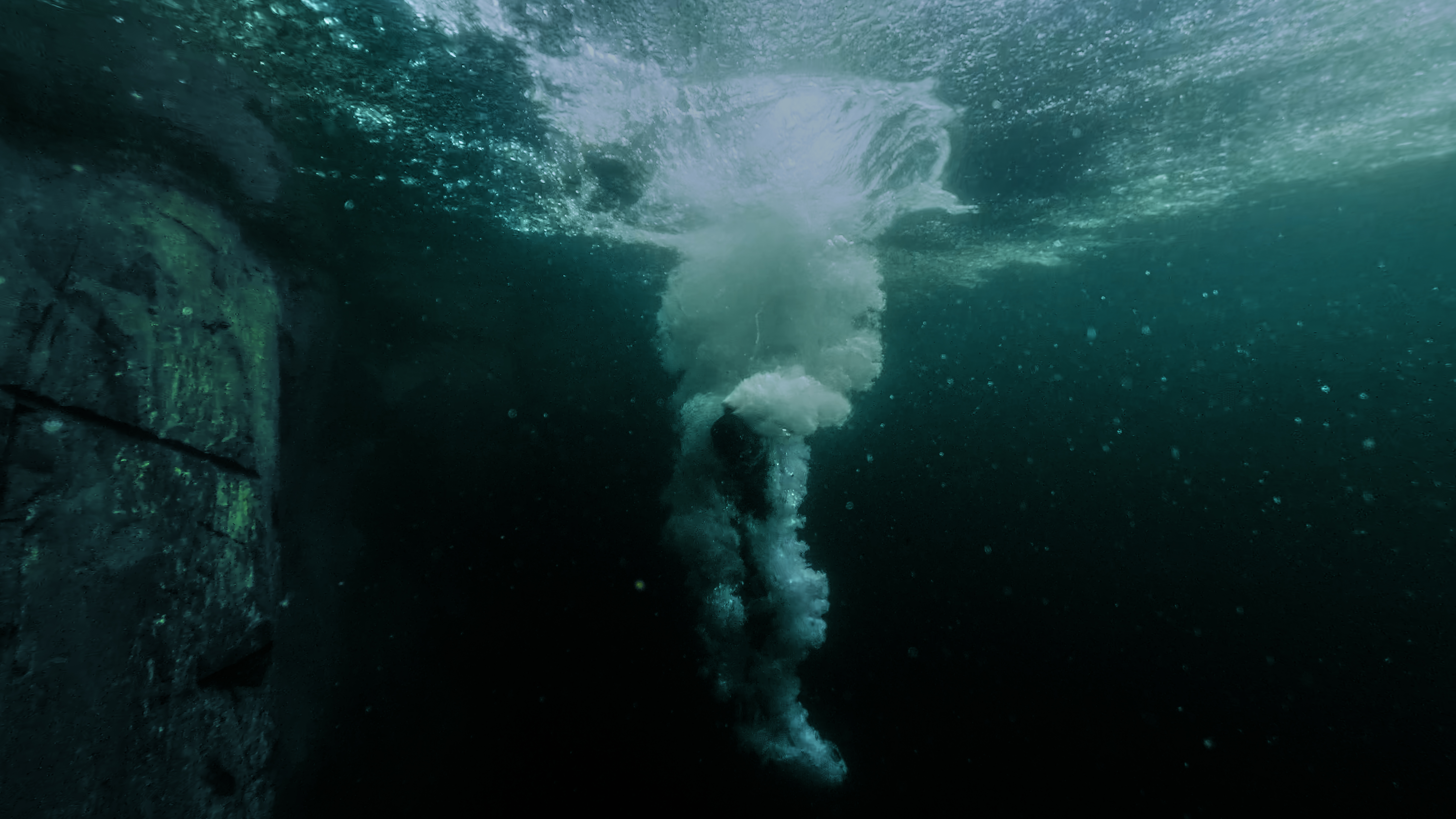 A person in a black wetsuit in the water places a hard-shell case on a metal beam.