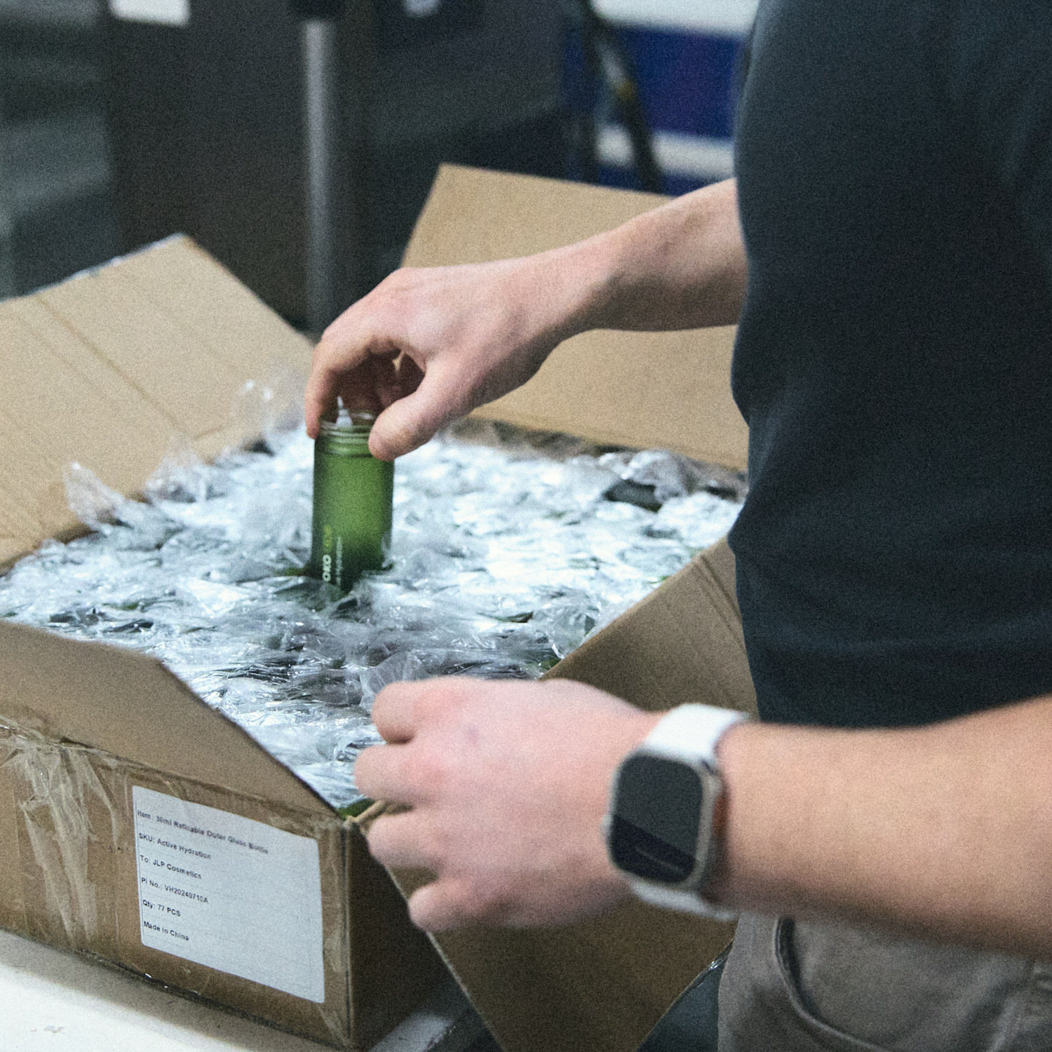 Person holding a green bottle, wearing black shorts, and a watch.
