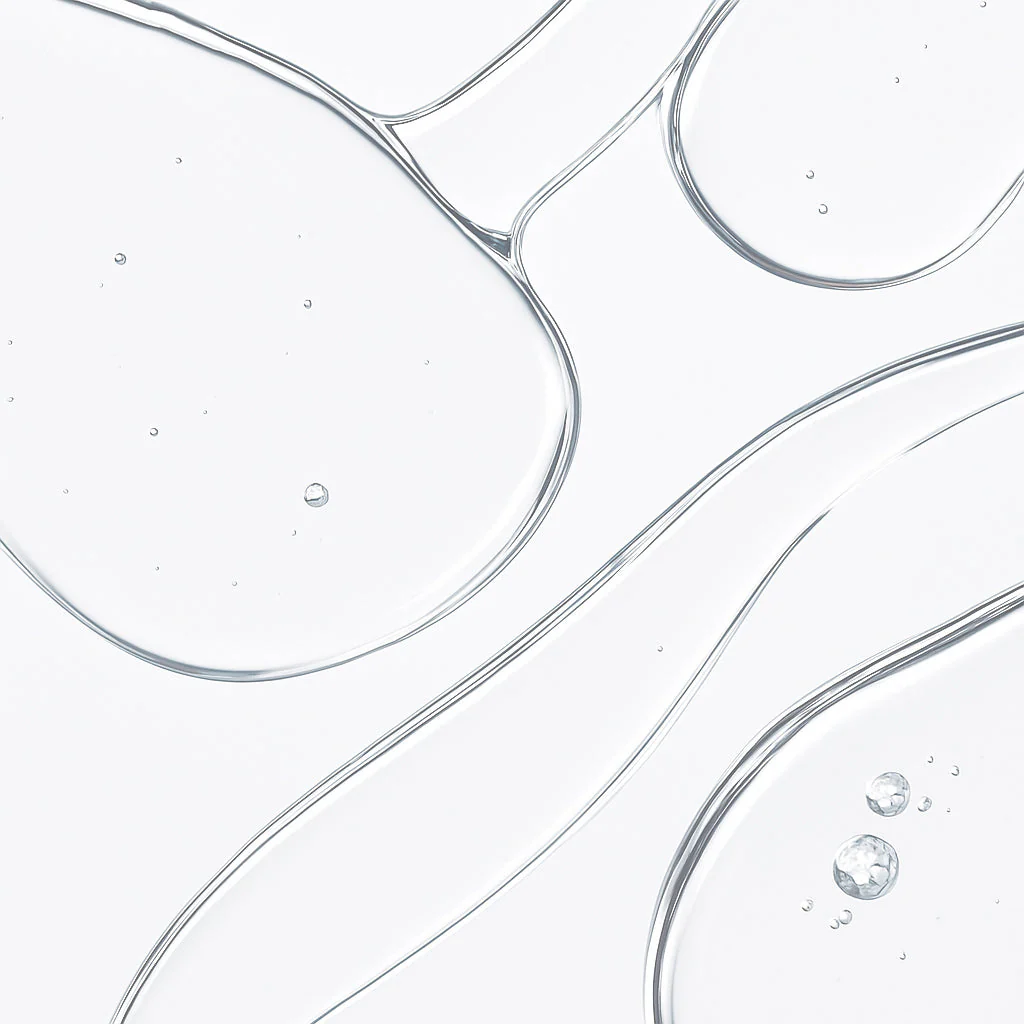 A macro photograph of a clear, viscous liquid with small bubbles on a white background.