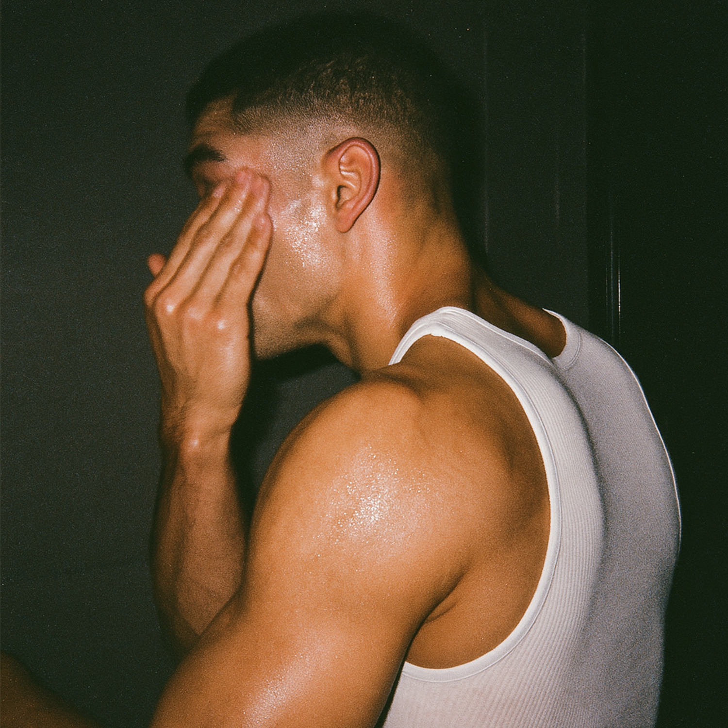 Man running on a forest trail wearing a cap and sleeveless shirt.