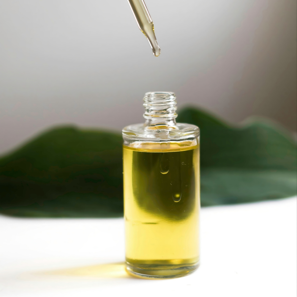 A drop of yellow oil falls from a glass dropper into a bottle with a green leaf behind it.