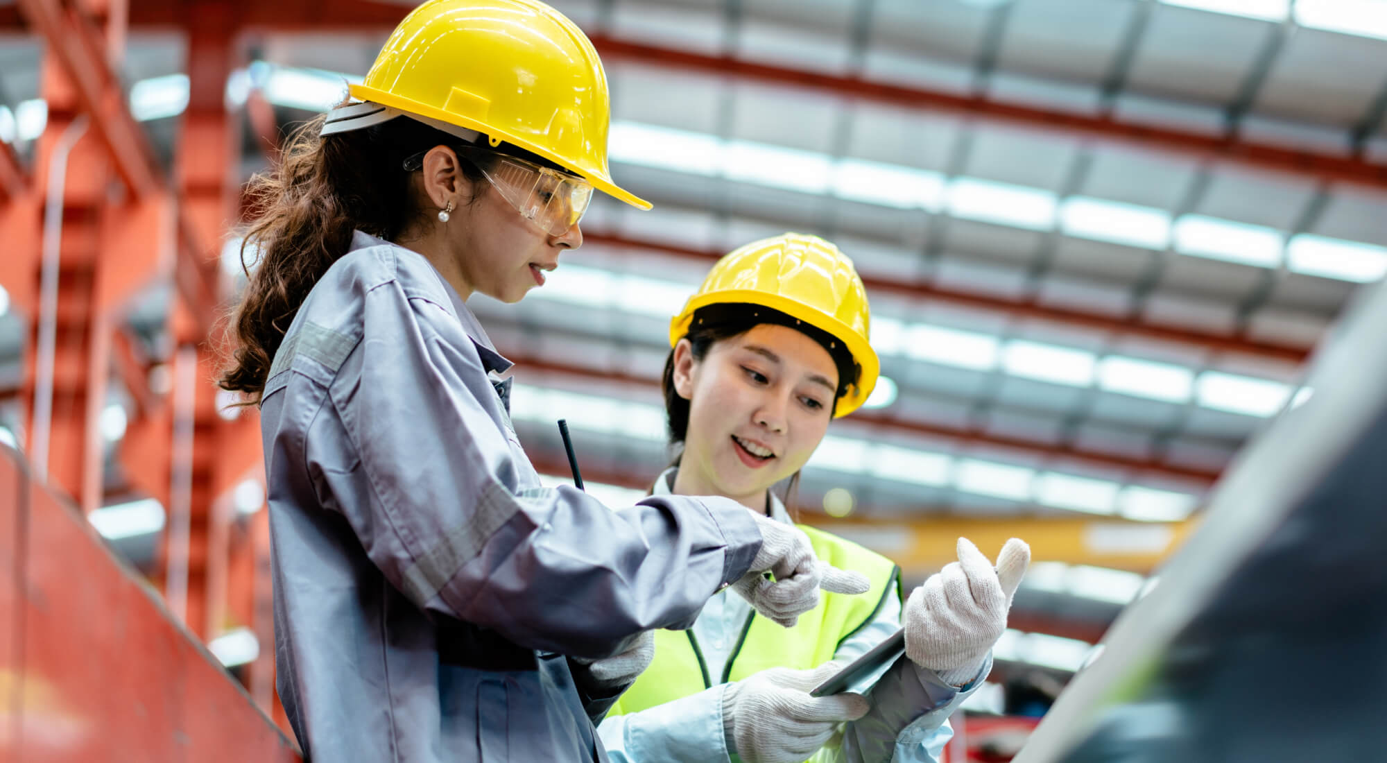 Deux travailleuses d’usine portant un casque de sécurité et de l’équipement de protection consultent une tablette ensemble.