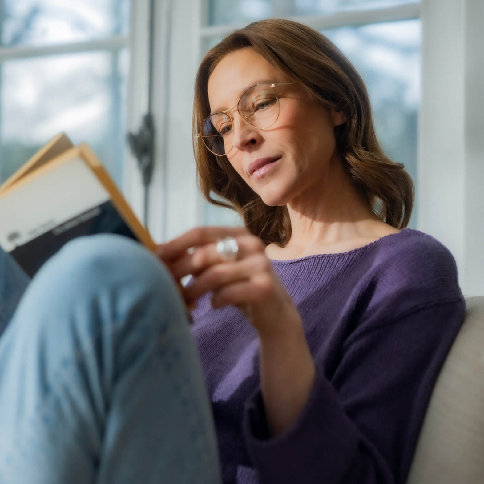 Woman wearing presbyopia corrective glasses reading a book comfortably on a couch