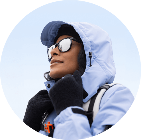 Une femme portant un manteau à capuchon bleu clair, des gants noirs et des lunettes de soleil miroir regarde vers le haut.