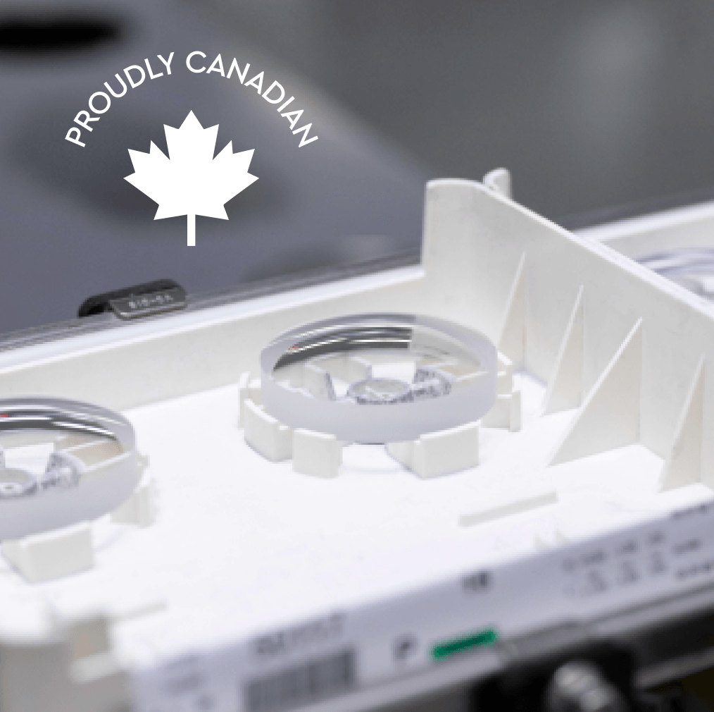 A close-up of optical components in a white manufacturing tray with a 'Proudly Canadian' logo overlaid.