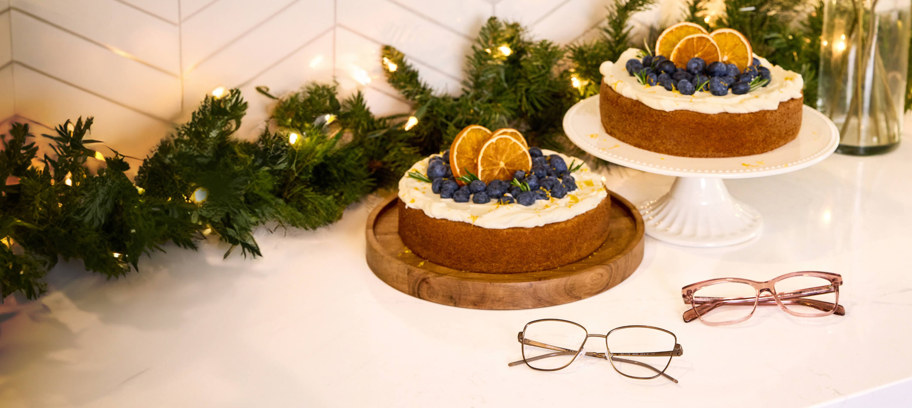 Two pairs of eyeglasses displayed beside holiday cakes on a table.
