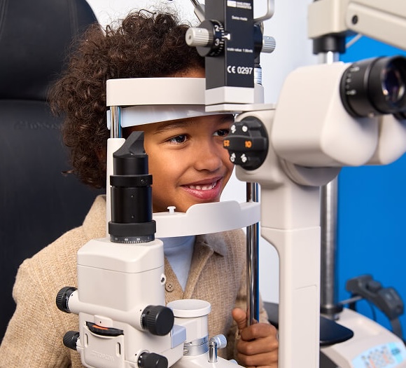 A smiling young child looks into an eye examination machine during an eye test.