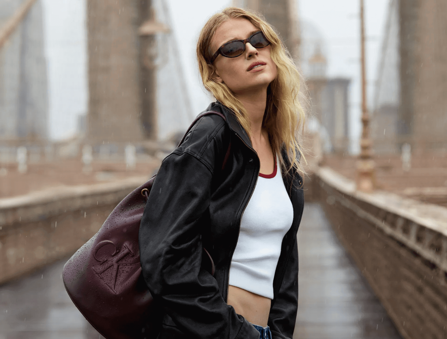 Woman wearing chic Calvin Klein sunglasses as she walks through the city’s bridge on a rainy day