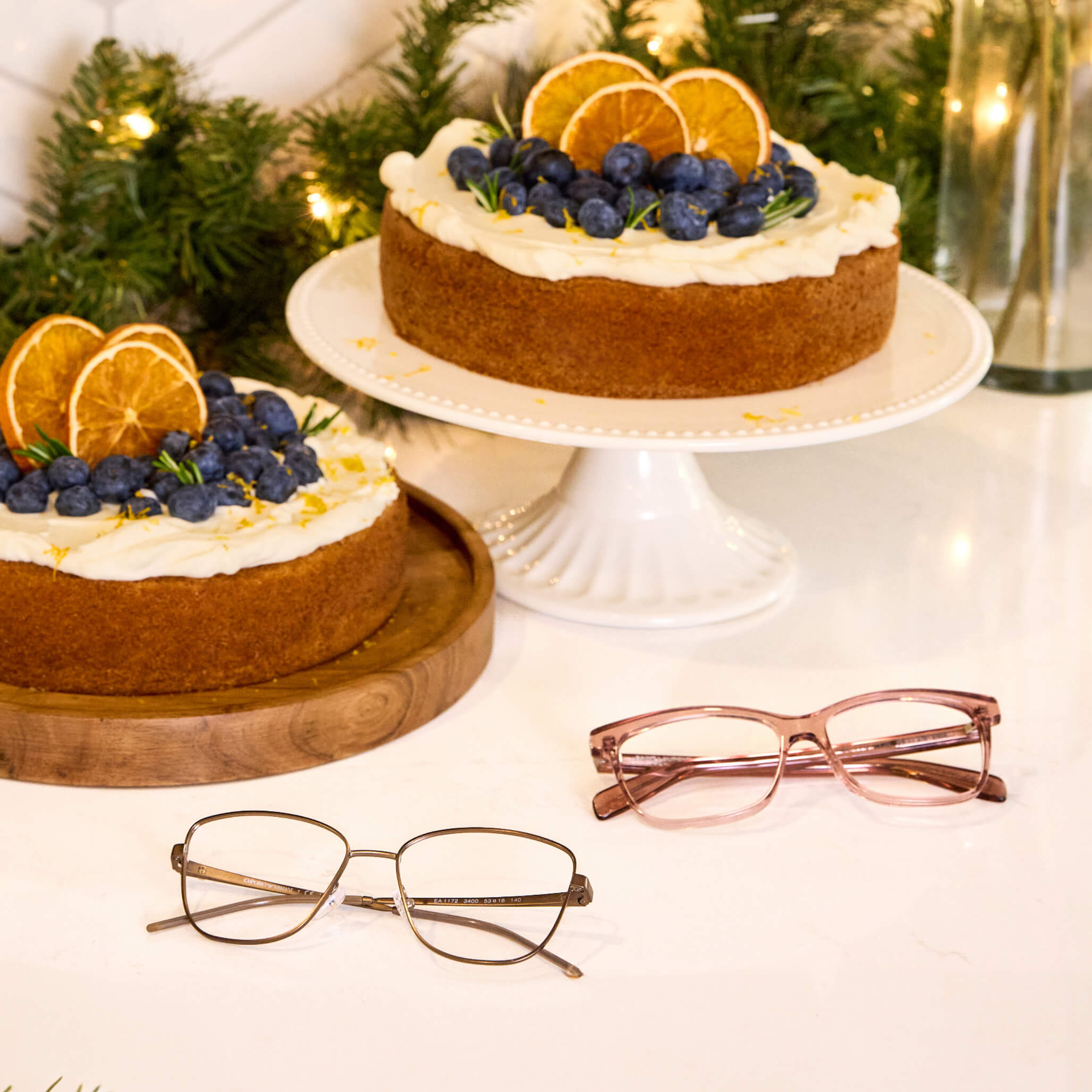 Two pairs of eyeglasses displayed beside holiday cakes on a table.