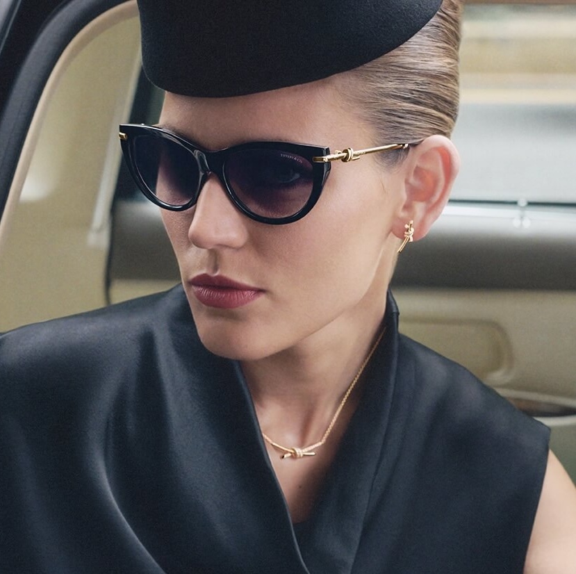 Woman in Tiffany sunglasses and black outfit sitting in a vehicle.