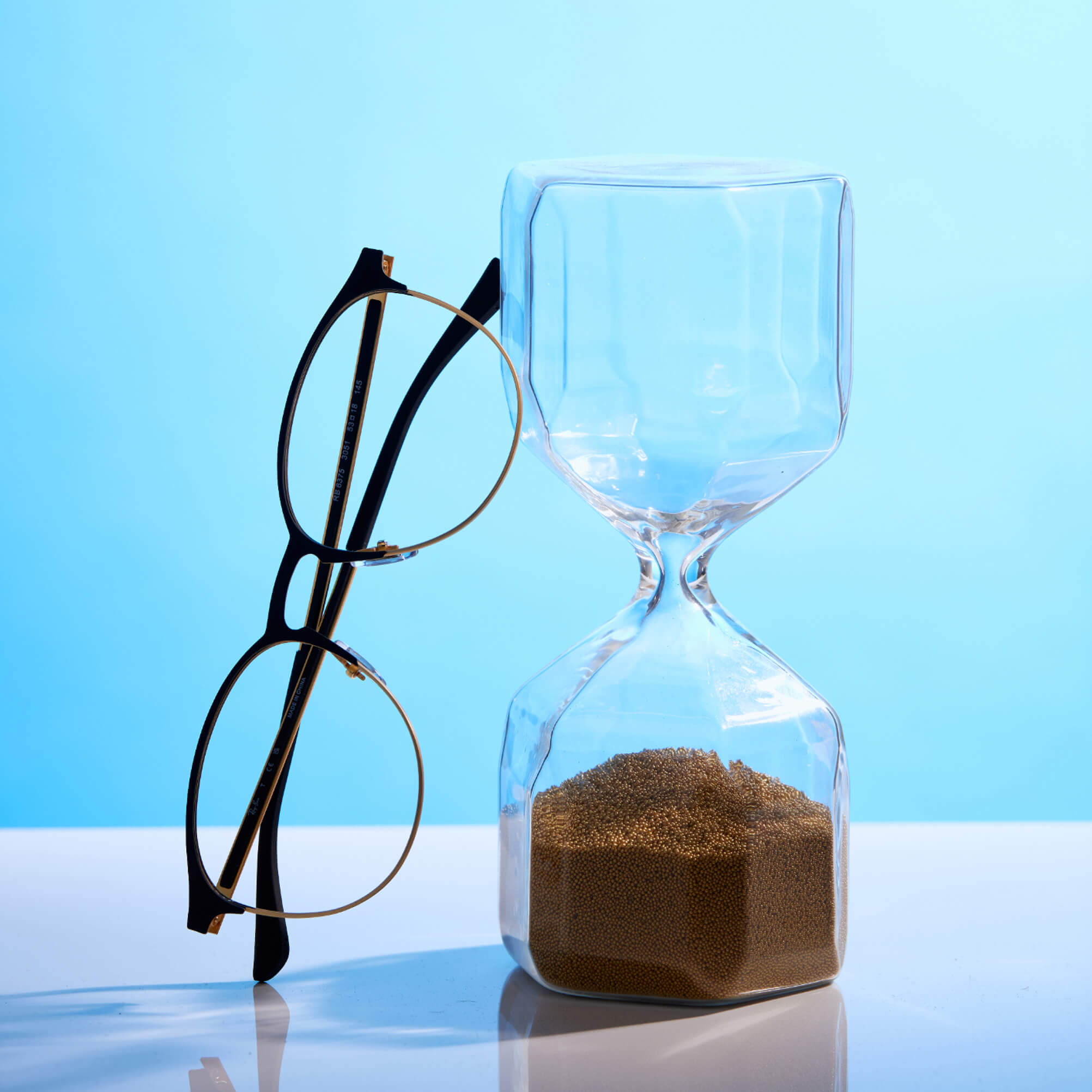 Glasses next to an hourglass, surrounded by a beautiful blue background.