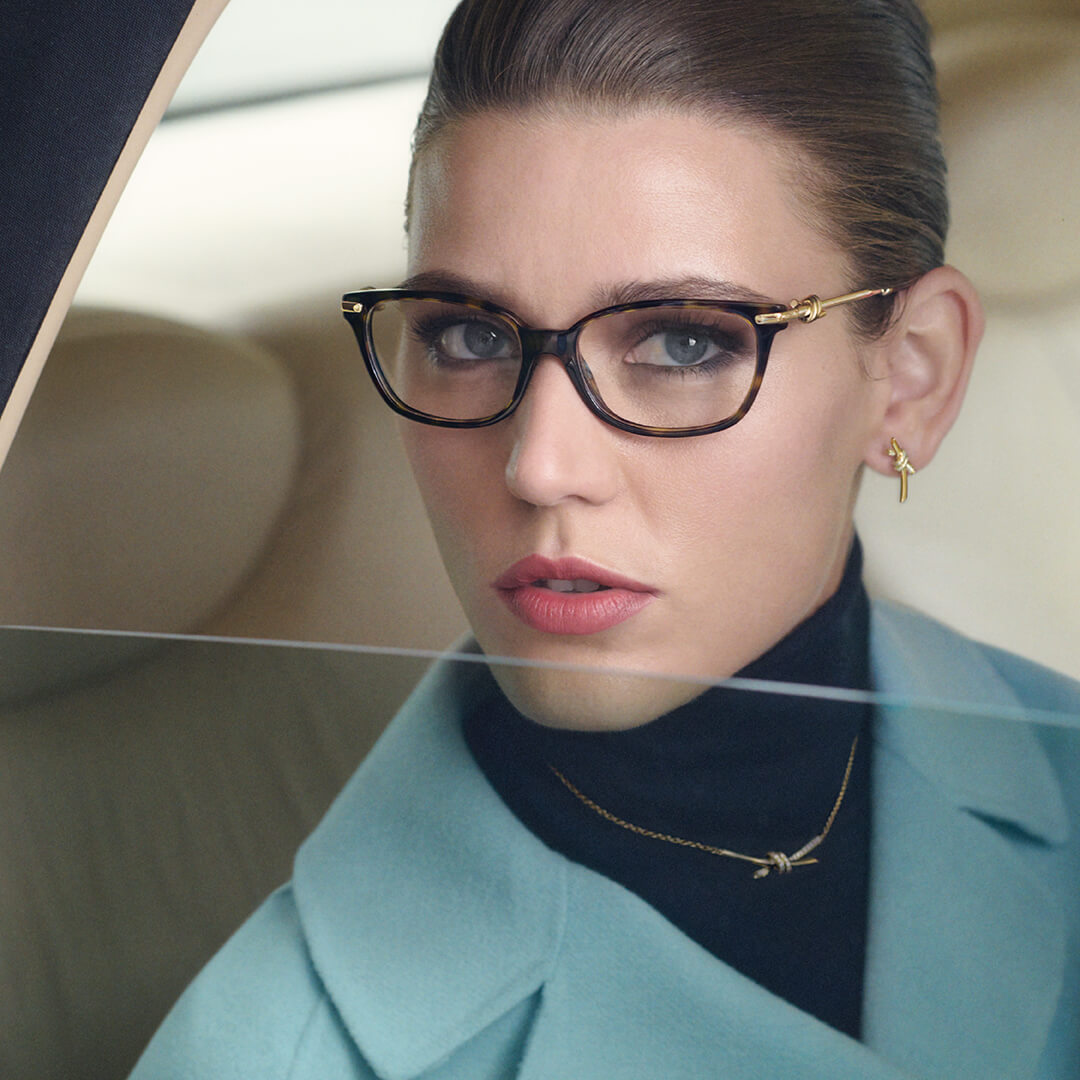 Woman wearing Tiffany glasses and a turquoise coat in a close-up portrait through a car window.