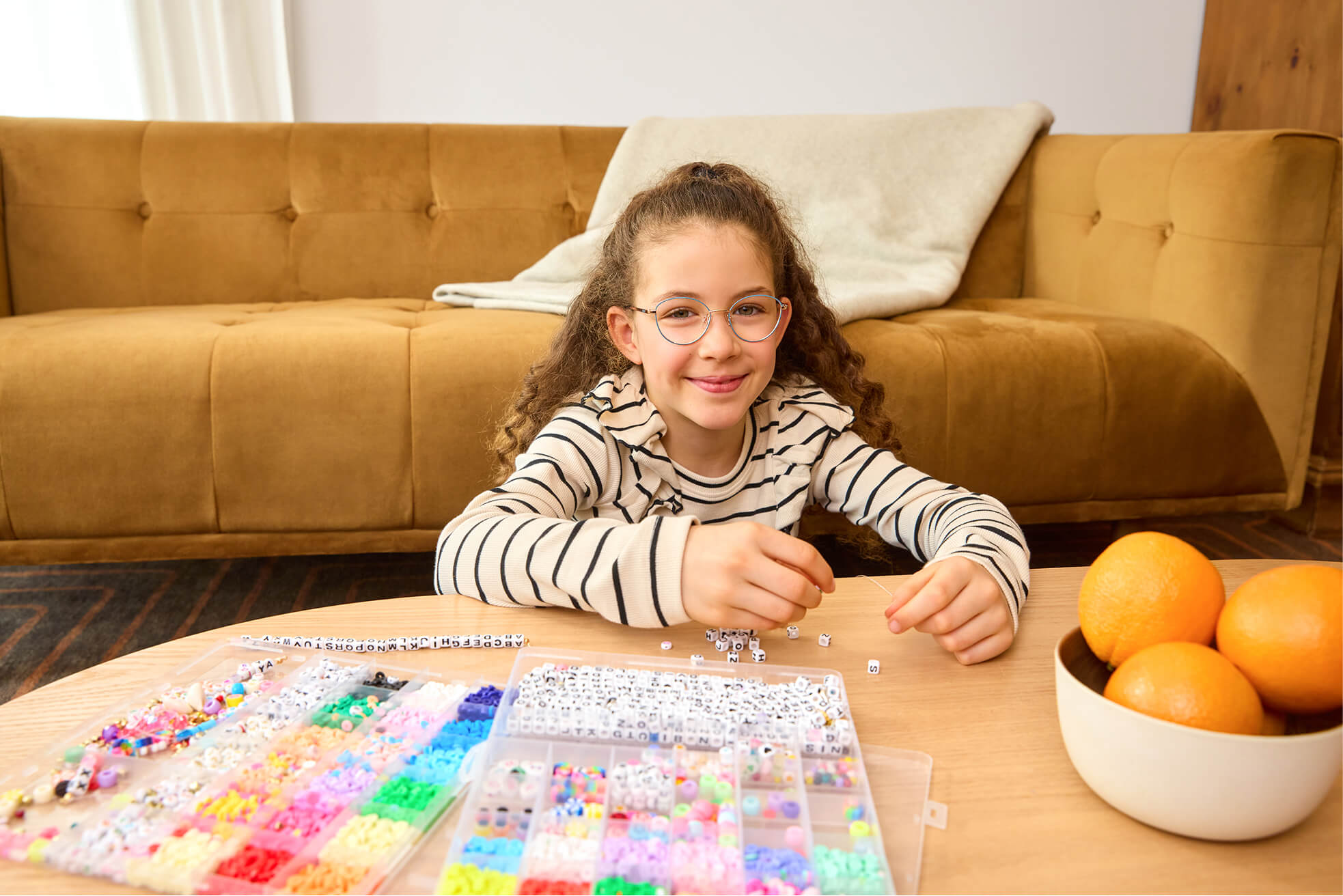 Happy girl making bead jewelry at a table, wearing glasses that address her myopia.