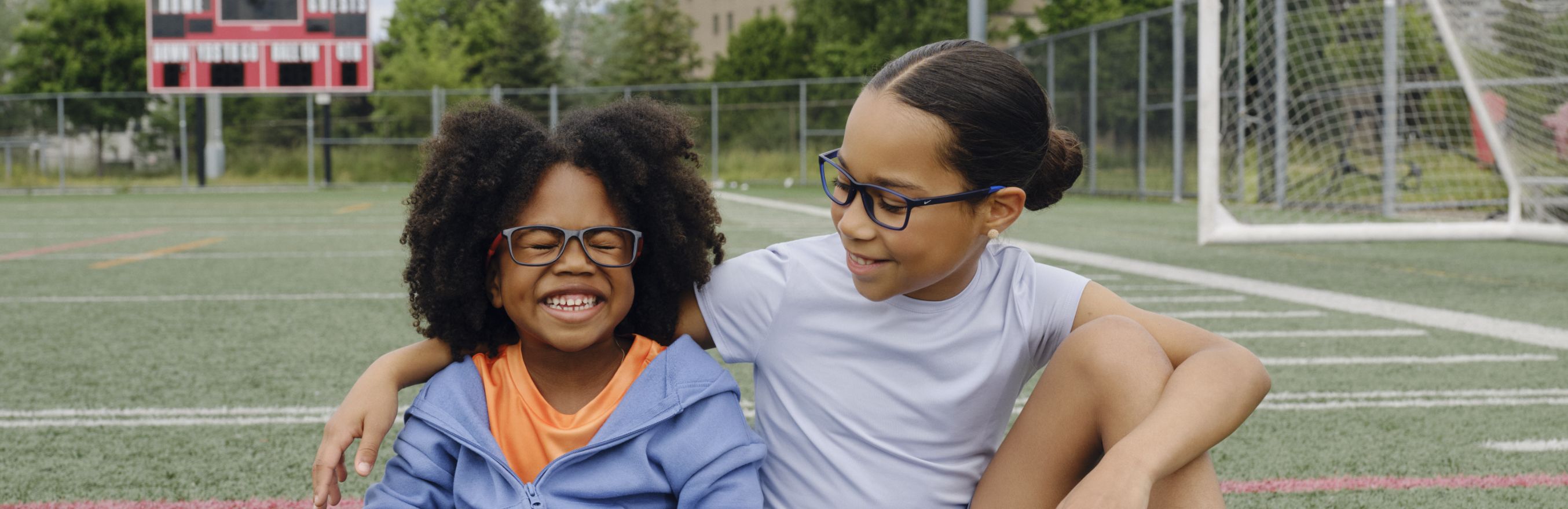 Two sisters hugging and sitting in a soccer field