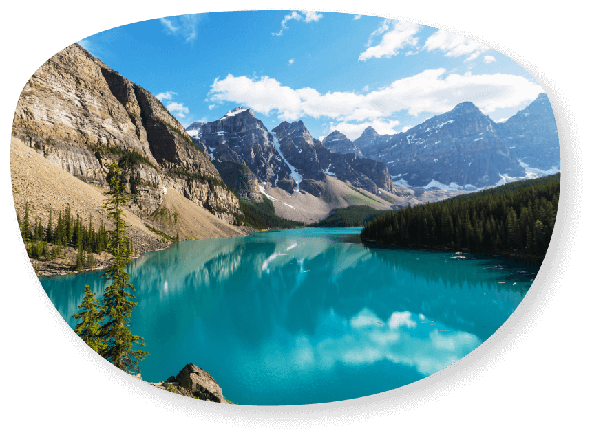 Lac turquoise vif au pied de montagnes rocheuses aux sommets enneigés, sous un ciel bleu.