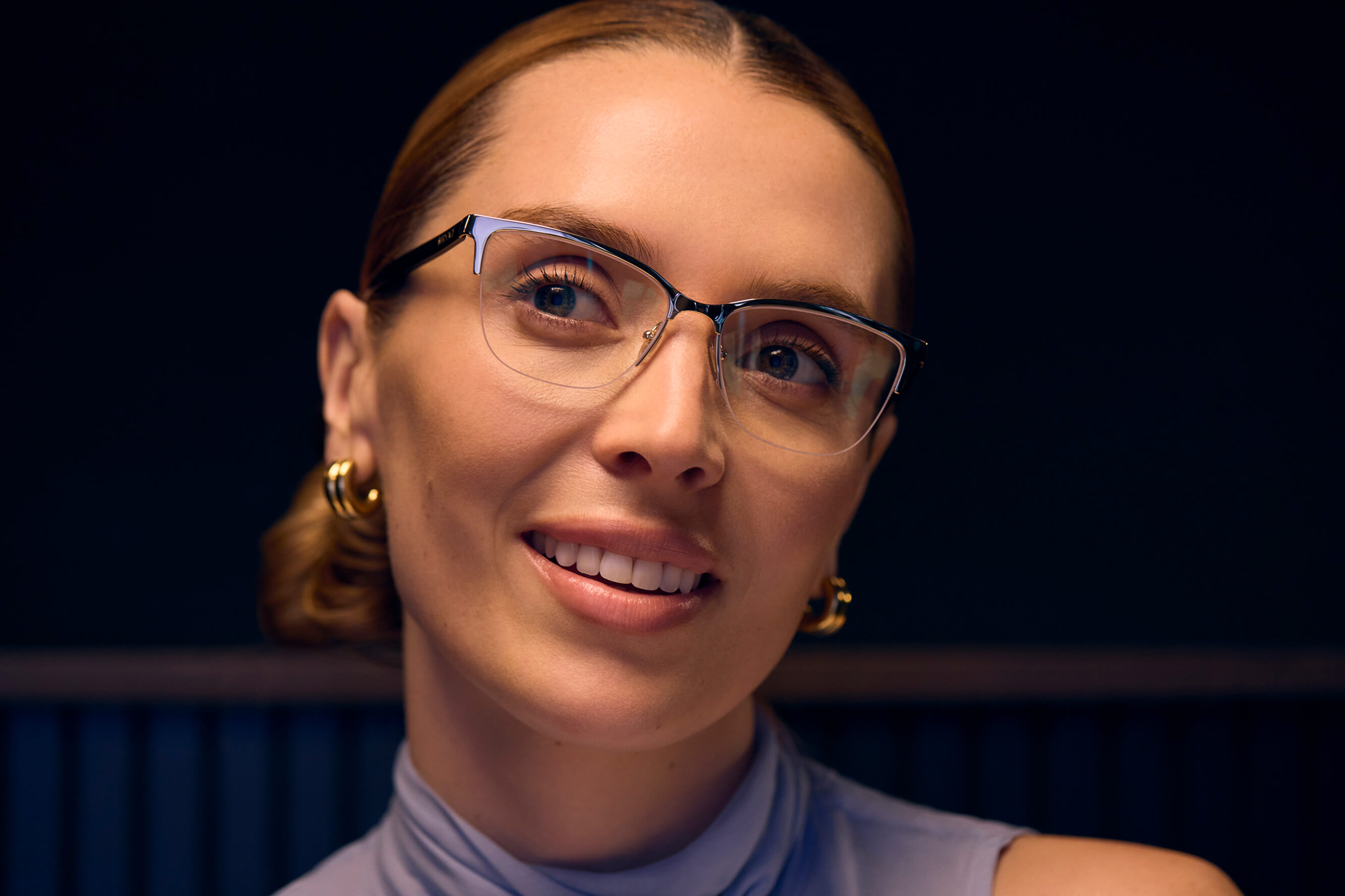 A close-up of a smiling woman wearing modern eyeglasses with her hair pulled back.